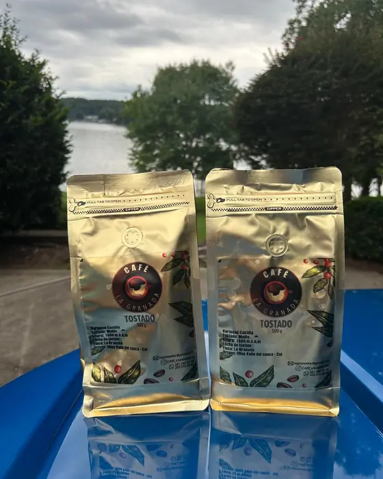 Dos bolsas doradas de Café La Granada frente a un lago